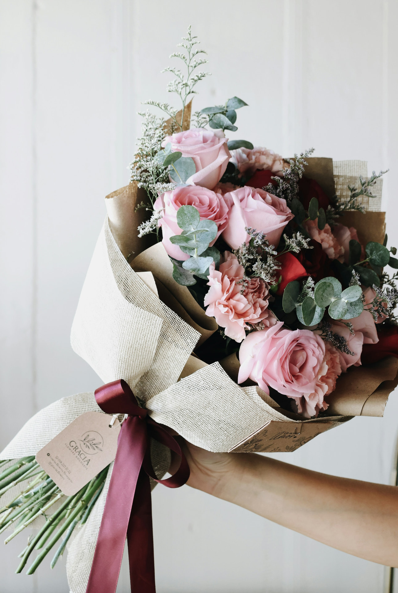 Hand-tied bouquet of pink roses, carnations, eucalyptus and dried accents wrapped in burlap